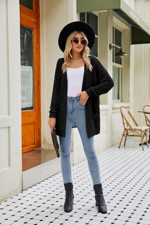 Black cable-knit cardigan with pockets and long sleeves, styled with a white top and jeans.