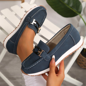 Dark blue slip-on loafers with gold and black buckle detail and contrast stitching.