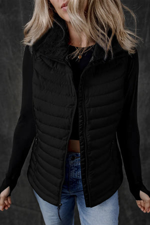 Black quilted puffer vest with fleece collar and zip front, worn over a black top.