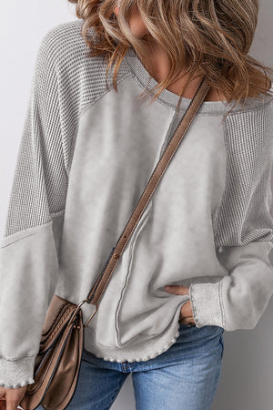 Gray waffle knit raglan sweatshirt with contrast sleeves and raw hem detail.