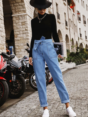 Belted high-waist light wash denim barrel trousers with cuffed hems.