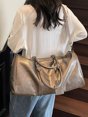 Textured metallic duffle bag in champagne color with detachable strap and handle.