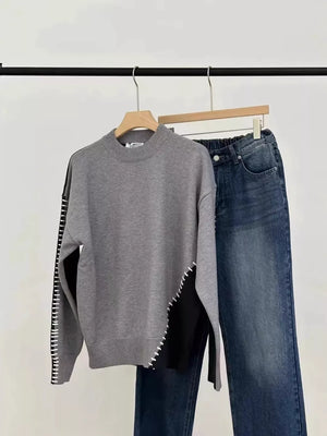 Gray mock neck sweater with black color block detail and contrast stitching, paired with denim jeans.