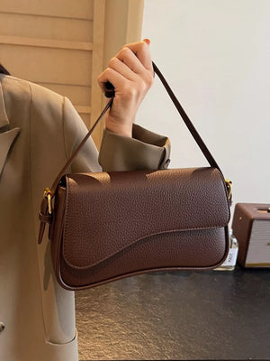 Sleek faux leather crossbody bag in coffee color with a curved flap and gold buckle detail.