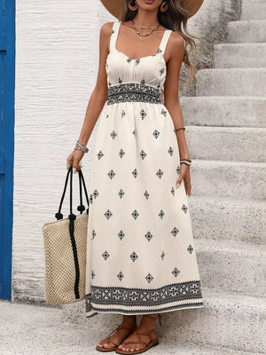 White midi dress with black geometric print, wide straps, smocked waist, and tiered hem.