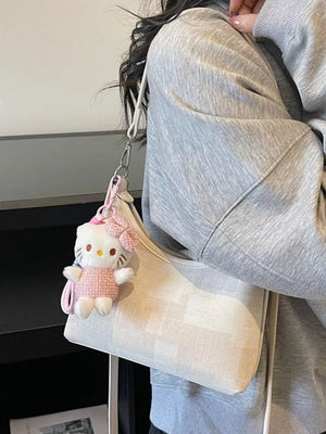Ivory crescent shoulder bag with a Hello Kitty charm and textured pattern.