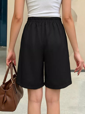 Black chino shorts with high waist and elastic waistband, styled with a white tank top and brown handbag.