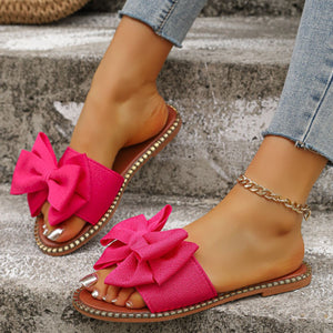 Fuchsia pink bowknot slide sandals with gold stud trim, worn with jeans and anklet.