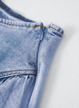 Medium wash denim mini skirt with asymmetrical ruffle detail and side zipper.