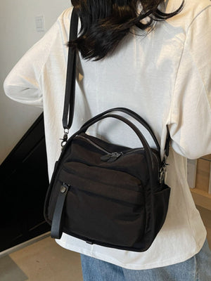 Black crossbody bag with decorative pull tab and dual top handles.