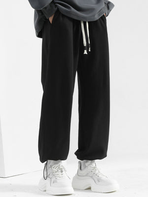 Men's black sweatpants with drawstring and loose fit, styled with white sneakers.