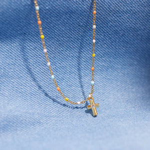 Gold necklace with rainbow beads and a small cross pendant with a clear stone.