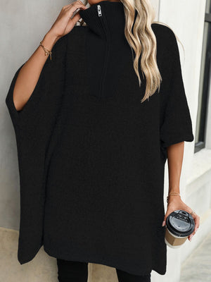 Black knit poncho with asymmetric cut, zip-neck, and short sleeves.