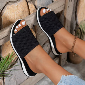 Black open-toe knit slide sandals with white soles and a gold ankle bracelet.