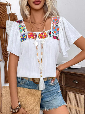 White embroidered square neck blouse with flutter sleeves and colorful floral details.
