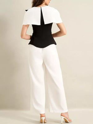 Black peplum top with white cape detail and white wide-leg pants.