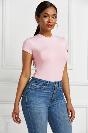 Blush pink crew neck short sleeve bodysuit with a smooth finish, paired with blue denim jeans.