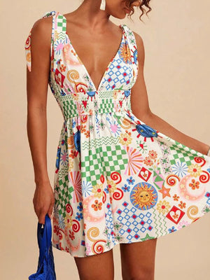 Playful printed mini dress with tied straps, V-neck, smocked waist, and a colorful patchwork pattern.
