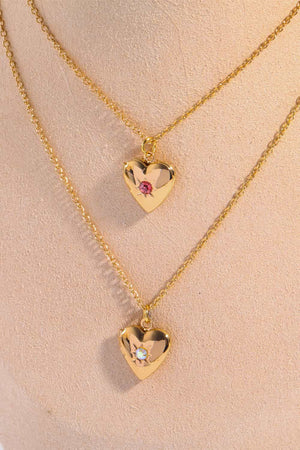 Gold heart locket necklaces with gemstone accents, one with a pink gemstone, the other with a clear gemstone.