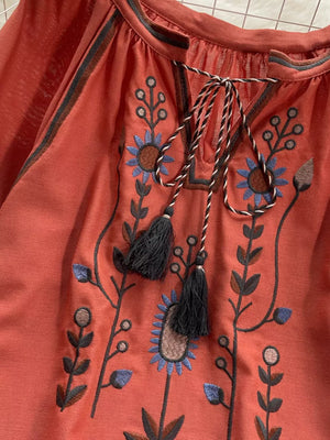 Orange red tie neck blouse with intricate floral embroidery and tassels.
