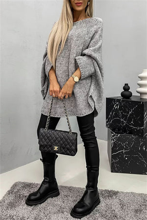 Gray knit sweater with cape sleeves, crew neck, and relaxed fit, styled with black pants and boots.