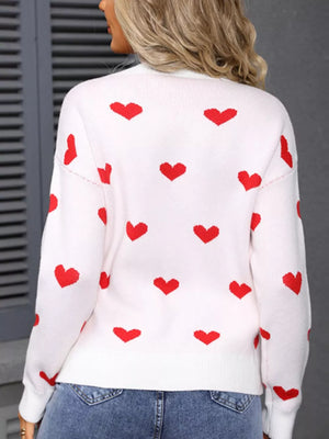 White knit sweater with red heart print, long sleeves, and crew neck.
