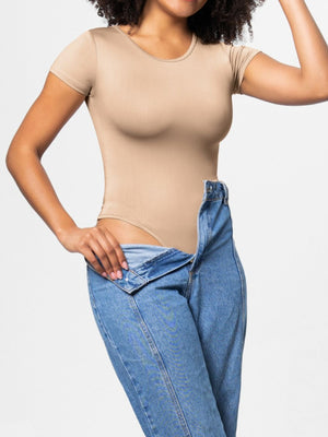 Tan short sleeve scoop neck bodysuit with a smooth finish, worn with jeans.