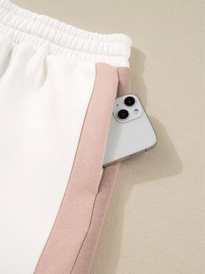 White cotton pajama shorts with blush pink color block detail and side pocket holding a phone.