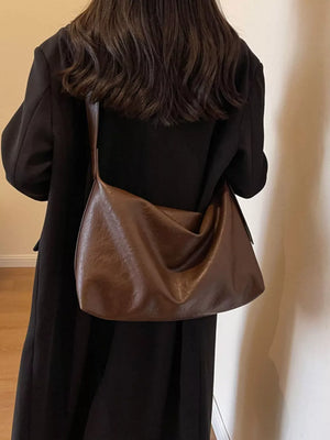 Brown leather shoulder bag with adjustable strap, worn with a black coat.
