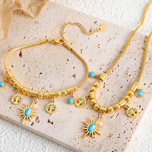 Gold celestial charm necklace with sunburst, tree of life, and turquoise charms.