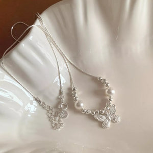 Silver necklace with pearl beads and a delicate butterfly charm.