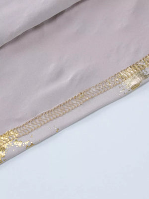 Cream maxi gown detail with abstract gold pattern and stitched hem.