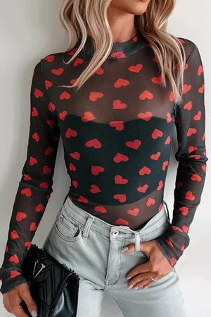 Black sheer mesh long sleeve top with red heart print, high neckline, worn with a black bandeau and light wash jeans.
