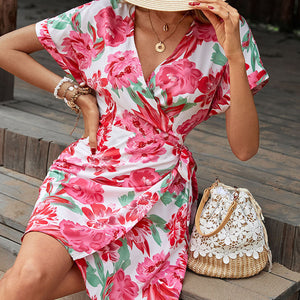 Floral wrap mini dress with flutter sleeves and a tie waist, styled with jewelry and a straw bag.