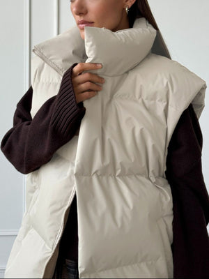 Padded puffer vest in Dust Storm with a high collar and zip front, layered over a dark sweater.