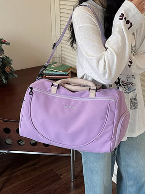 Purple duffle bag with adjustable strap and embroidered detail, worn by a woman.