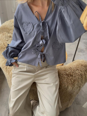 Gray tie-front blouse with heart appliqué details and ruffled cuffs.