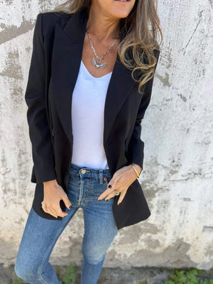 Black double-breasted blazer with sculpted lapels worn open over a white tank top and jeans.