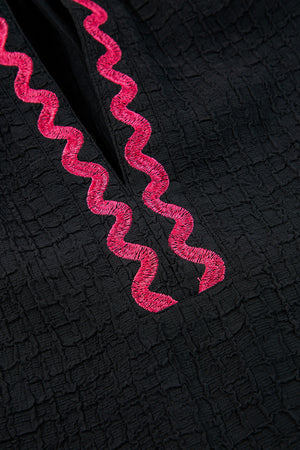 Black blouse with textured fabric and pink embroidered zigzag neckline detail.