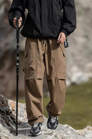 Men's brown cargo pants with multiple pockets and drawstring waist, styled with hiking gear.