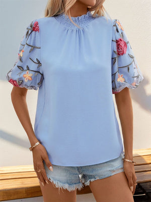 Light blue blouse with floral embroidered organza puff sleeves and ruffled neckline.