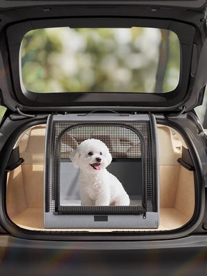 Gray pet carrier with mesh windows and a white dog inside, placed in a car trunk.