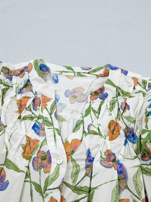 Cotton V-neck shirt with vibrant floral print, pleats, and button detail.
