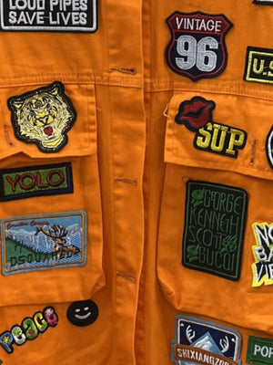 Orange denim trucker jacket with embroidered patches including a tiger, lips, and text.