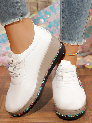 White wedge sneakers with colorful rhinestone embellishments on the sole.