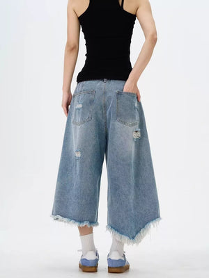 Distressed light wash denim wide-leg jeans with raw hem and cropped length.