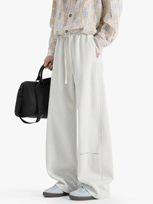 Casual wide-leg sweatpants in ivory with drawstring and subtle text detail.