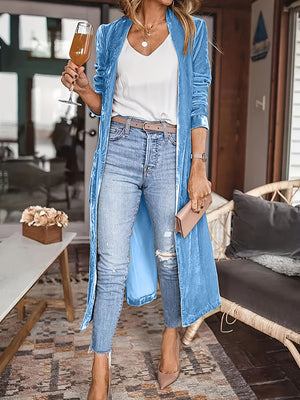 Blue velvet duster coat with fluid silhouette, open front, long sleeves, worn with jeans and heels.