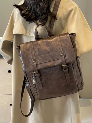Brown vintage-inspired pu leather flap backpack with brass hardware and adjustable straps.