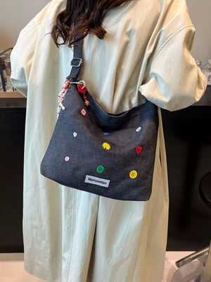 Dark blue denim crossbody bag with colorful button and heart embroidery and adjustable strap.